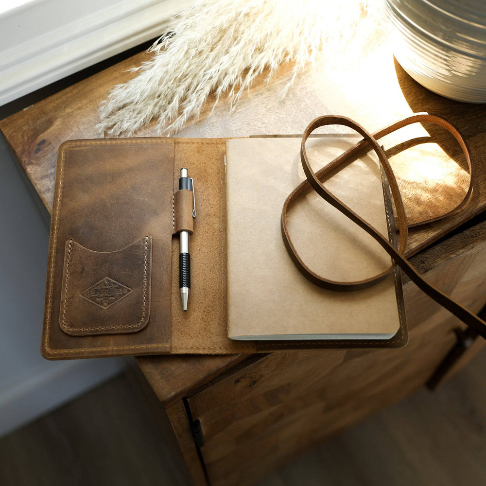 [lifestyle] An open leather journal resting on a wooden table.